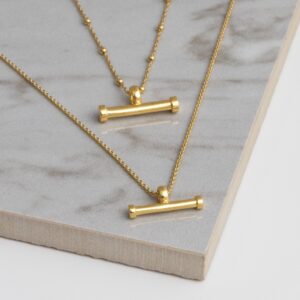 Gold plated Silver sterling silver T-bar necklace on a grey tile background, showing fine gold sterling silver ball chain and horizontal bar pendant.
