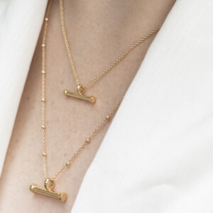 Small and large Minimalist Gold Plated sterling silver T-bar horizontal pendant necklace with a ball chain, worn around the neck and styled with a white blouse.