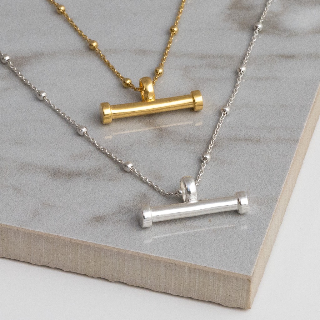 Gold plated and Silver sterling silver T-bar necklace on a grey tile background, showing fine sterling silver ball chain and small and large horizontal bar pendant.