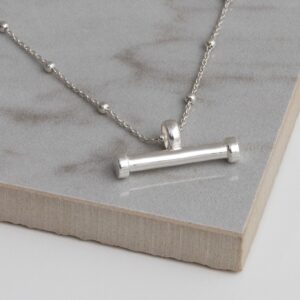 Silver sterling silver T-bar necklace on a grey tile background, showing fine gold sterling silver ball chain and small and large horizontal bar pendant.
