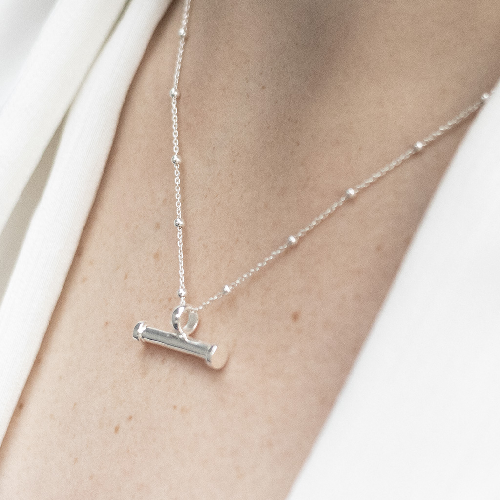 Minimalist sterling silver T-bar horizontal pendant necklace with a ball chain, worn around the neck and styled with a white blouse.