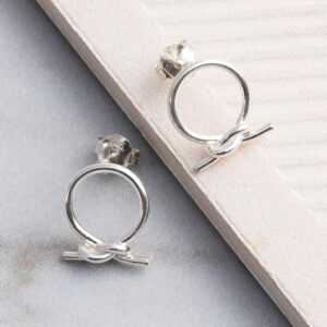 Sterling silver circle knot stud earrings with a polished finish, shown on a tile background.