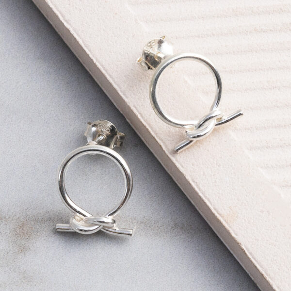 Sterling silver circle knot stud earrings with a polished finish, shown on a tile background.