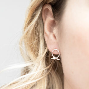 Sterling silver circle knot stud earrings with a polished finish, worn on a model with blonde curly hair.