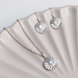 Sterling silver Mother of Pearl sun disc earrings and necklace set on a shell background.