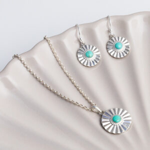 Sterling silver Turquoise sun disc earrings and necklace set set on a shell background.