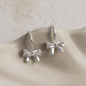 Sterling Silver Bow Drop Earrings on a wavy creamy background.