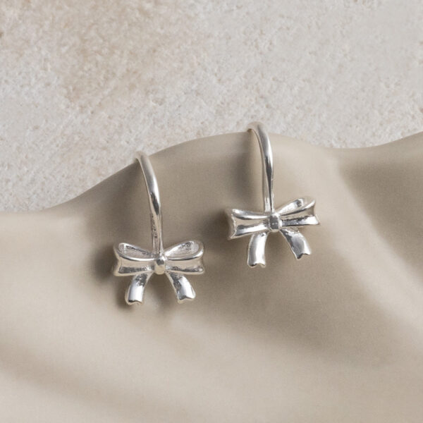 Sterling Silver Bow Drop Earrings on a wavy creamy background.