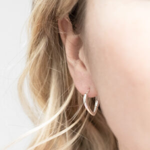 Sterling silver pear-shaped hoop earrings with a smooth, polished finish, worn by a model with blonde curly hair.