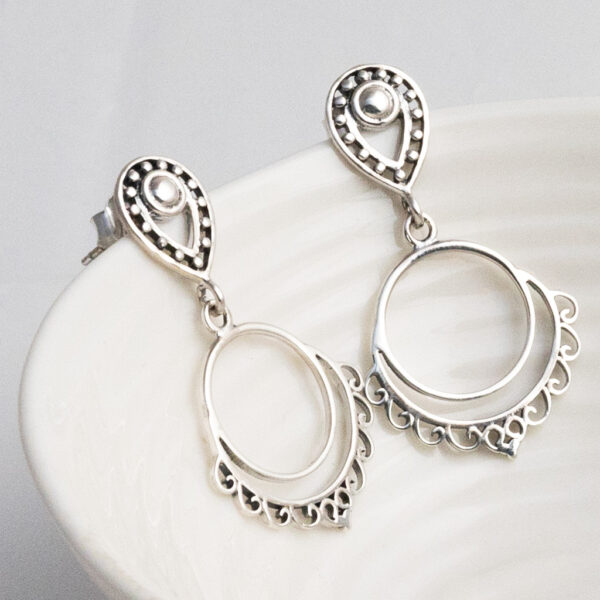 Sterling silver Moroccan-style teardrop stud earrings with delicate dangly design and intricate patterns on a white lined dish as a prop.
