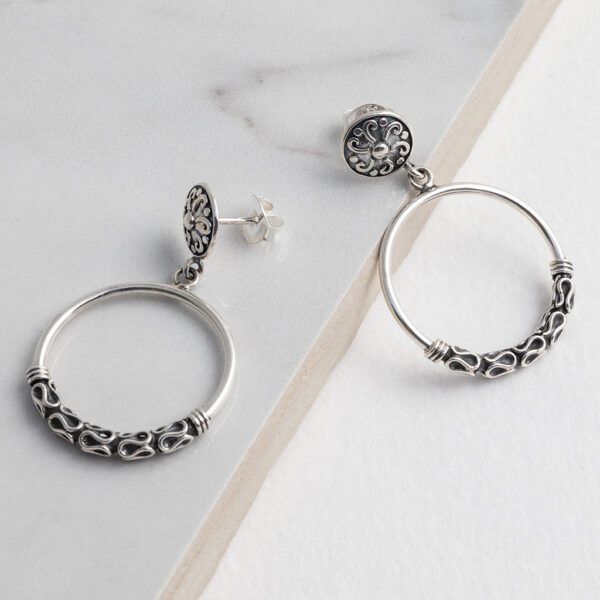 Sterling silver Java-inspired dangly hoop stud earrings with intricate detailing and a contemporary boho design on a grey title background.