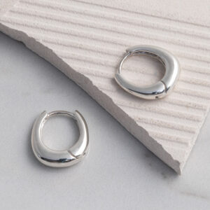 Sterling silver oval shaped hoop earrings with a smooth, polished finish, displayed on a tile background.