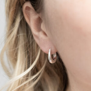 Sterling silver oval shaped hoop earrings with a smooth, polished finish, worn by a model with curly blonde hair.