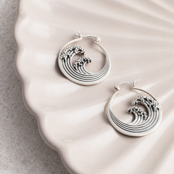Sterling silver hoop earrings inspired by the iconic Great Wave off Kanagawa, featuring intricate oxidised detailing to highlight the wave’s movement and texture on a cream shell background.