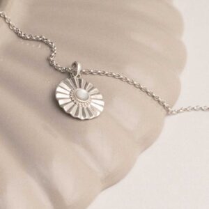 Sterling silver Mother of Pearl sun disc necklace on a white and shell background.