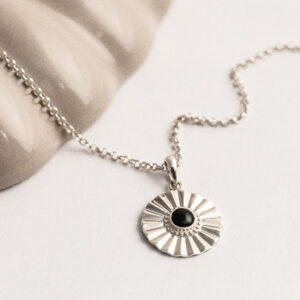 Sterling silver Onyx sun disc necklace on a white and shell background.