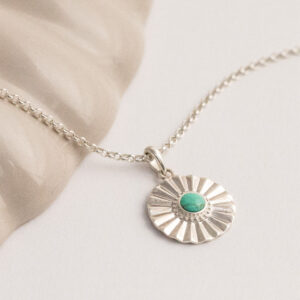 Sterling silver Turquoise sun disc necklace set on a white and shell background.