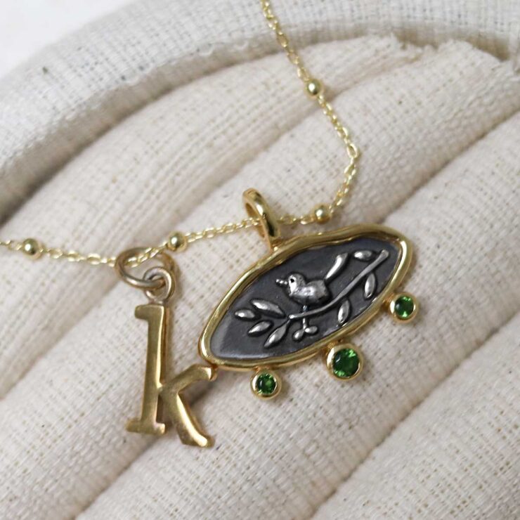 Gold Plated Sterling Silver Hieroglyphics Necklace with letter initial charm K on beige fabric background.