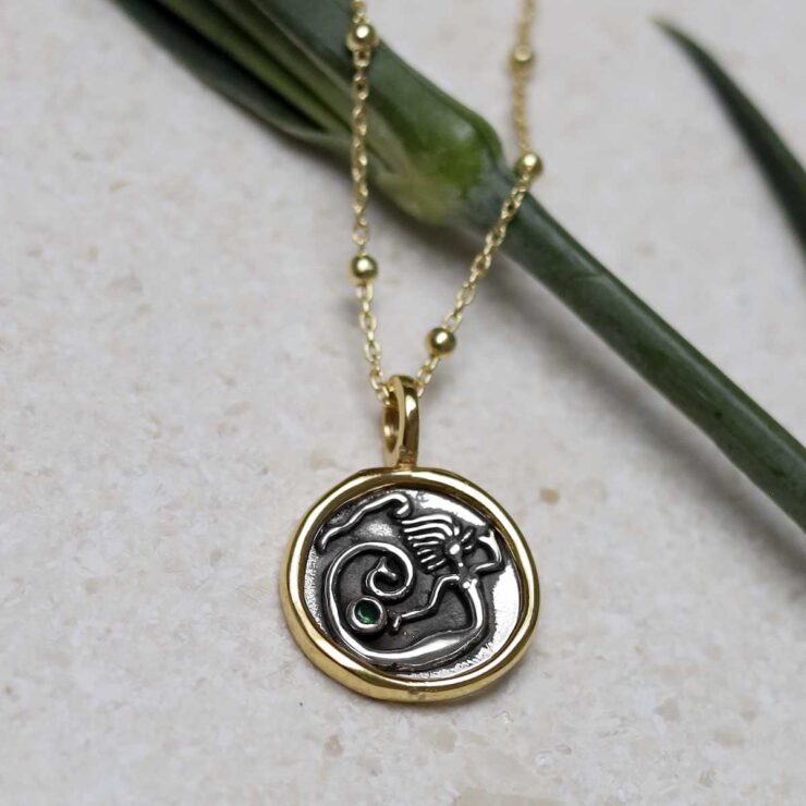 Gold Plated Sterling Silver Mermaid Necklace on beige background with green stem leaf.