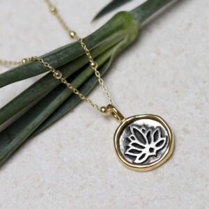 Gold Plated Sterling Silver Lotus Necklace on beige fabric background.