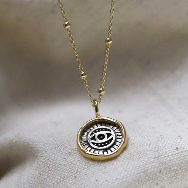 Gold Plated Sterling Silver Evil Eye Round Necklace on beige fabric background.