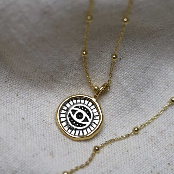 Gold Plated Sterling Silver Evil Eye Round Necklace on beige fabric background.