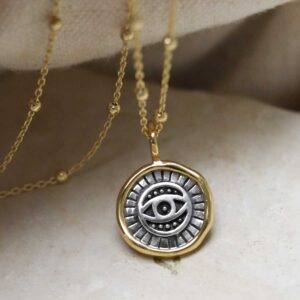 Gold Plated Sterling Silver Evil Eye Round Necklace on beige fabric background.