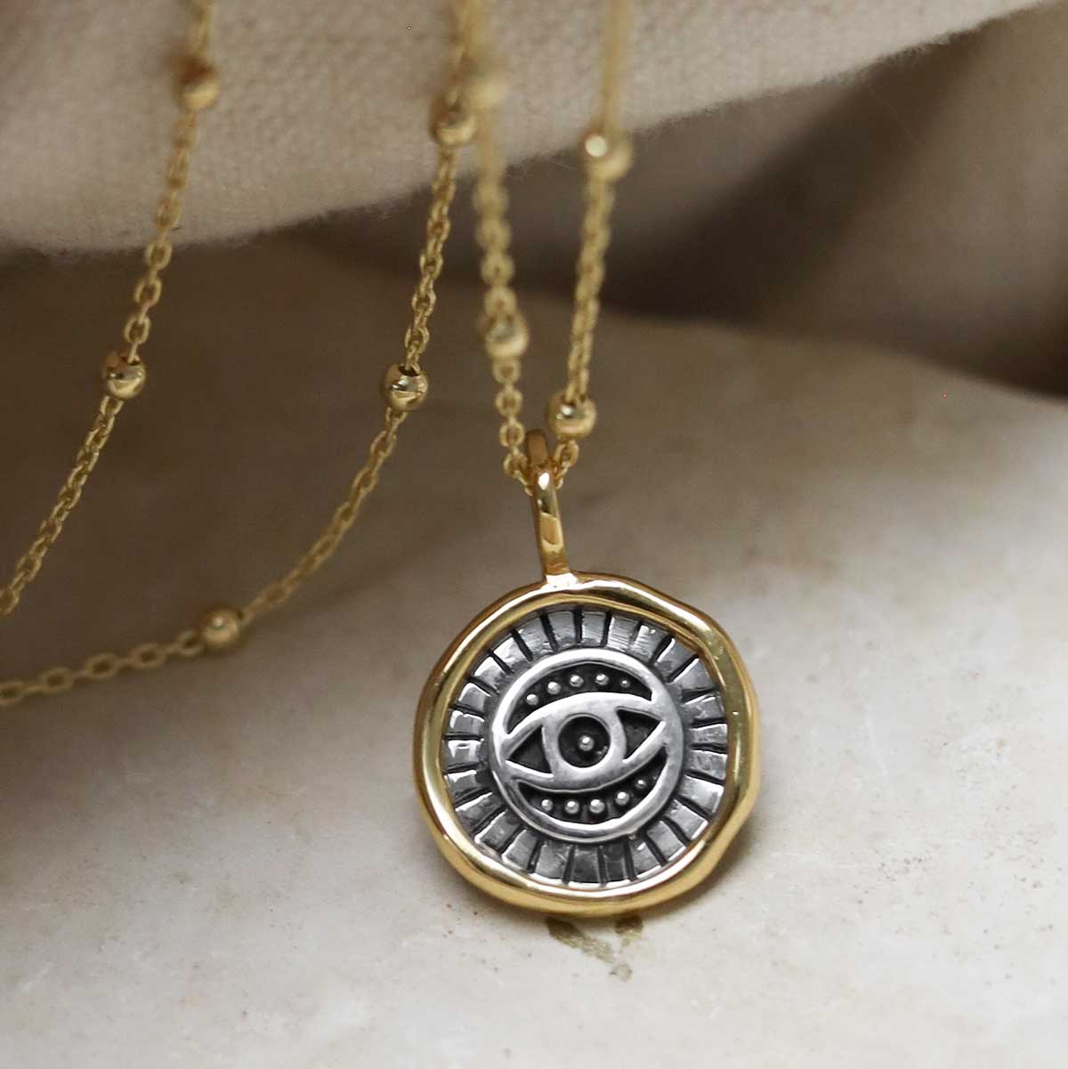 Gold Plated Sterling Silver Evil Eye Round Necklace on beige fabric background.