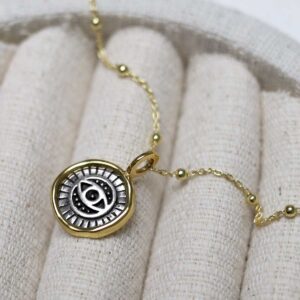 Gold Plated Sterling Silver Evil Eye Round Necklace on beige fabric background.