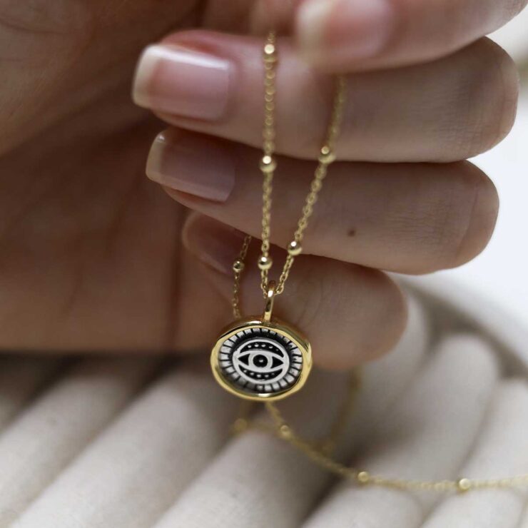 Gold Plated Sterling Silver Evil Eye Round Necklace on beige fabric background.