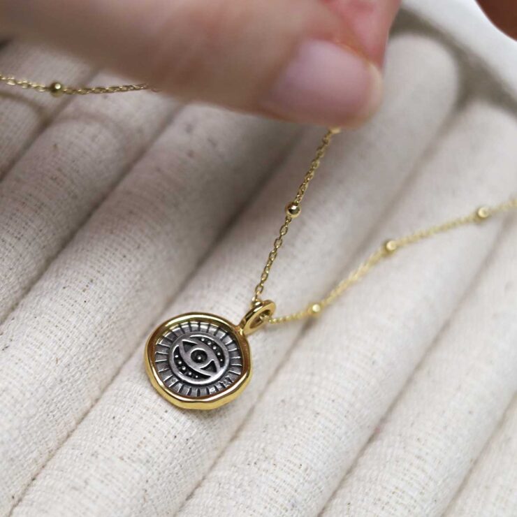 Gold Plated Sterling Silver Evil Eye Round Necklace on beige fabric background.