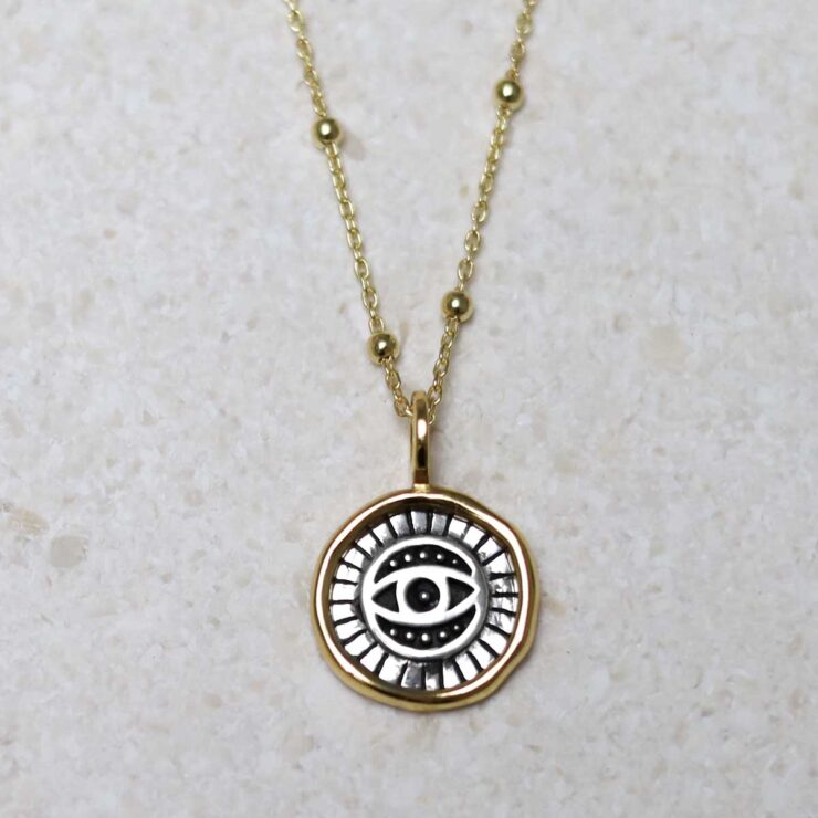 Gold Plated Sterling Silver Evil Eye Round Necklace on beige fabric background.