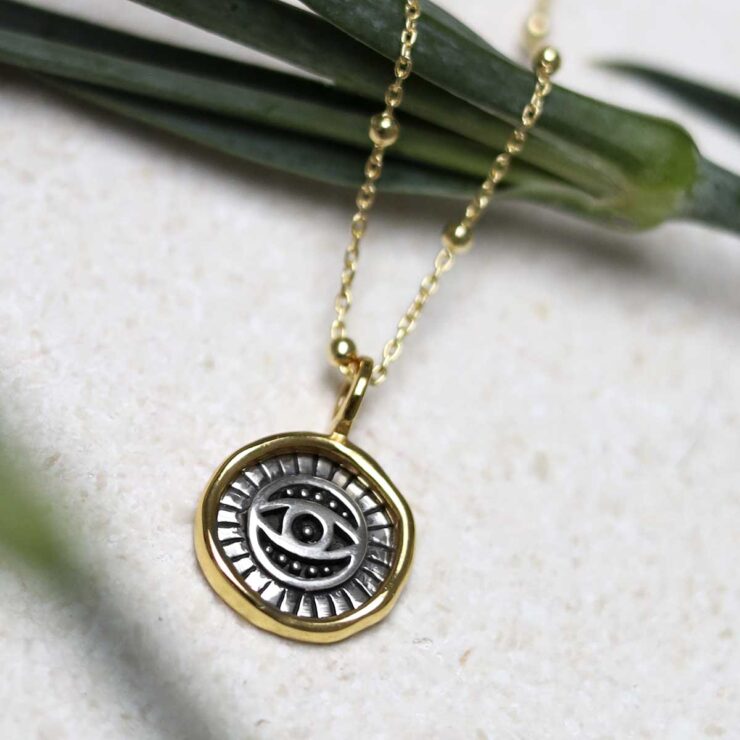 Gold Plated Sterling Silver Evil Eye Round Necklace on beige fabric background.