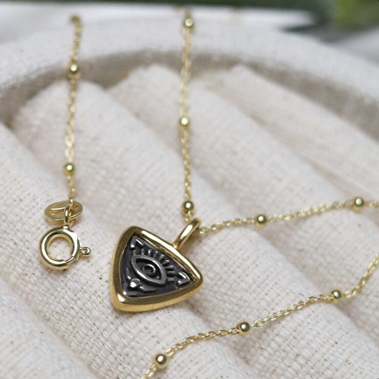 Gold Plated Sterling Silver Evil Eye Necklace on beige fabric background.
