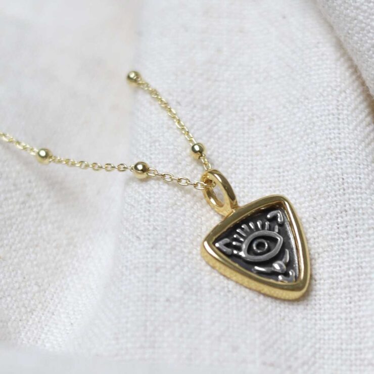 Gold Plated Sterling Silver Evil Eye Necklace on beige fabric background.
