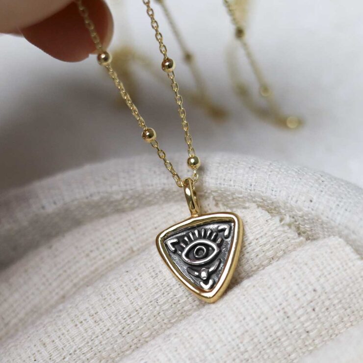 Gold Plated Sterling Silver Evil Eye Necklace on beige fabric background.