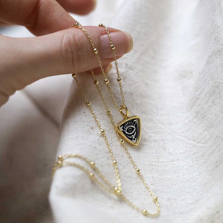 Gold Plated Sterling Silver Evil Eye Necklace on beige fabric background.