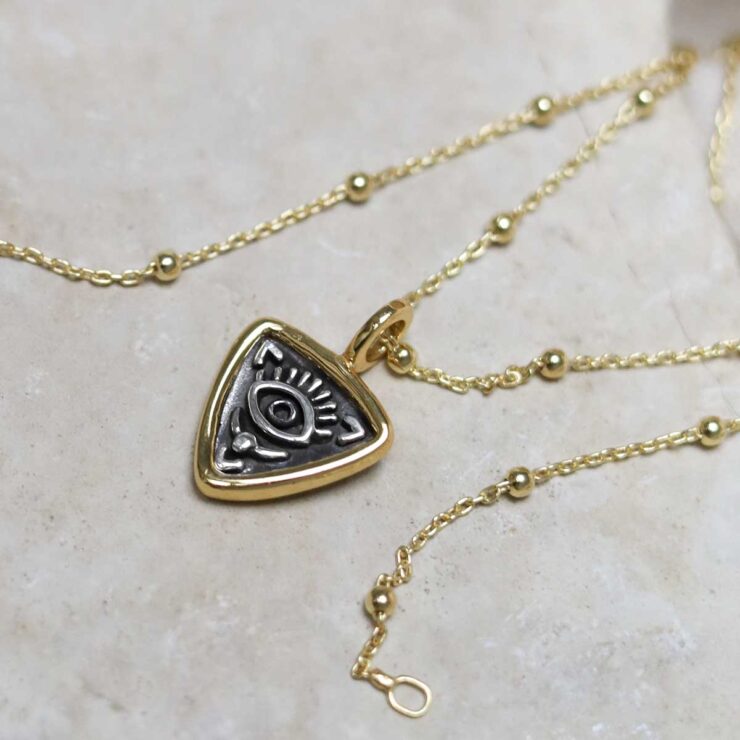 Gold Plated Sterling Silver Evil Eye Necklace on beige fabric background.