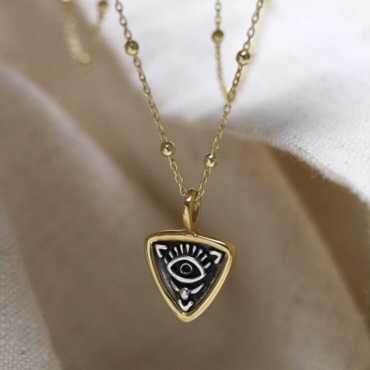Gold Plated Sterling Silver Evil Eye Necklace on beige fabric background.
