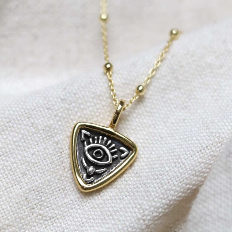 Gold Plated Sterling Silver Evil Eye Necklace on beige fabric background.